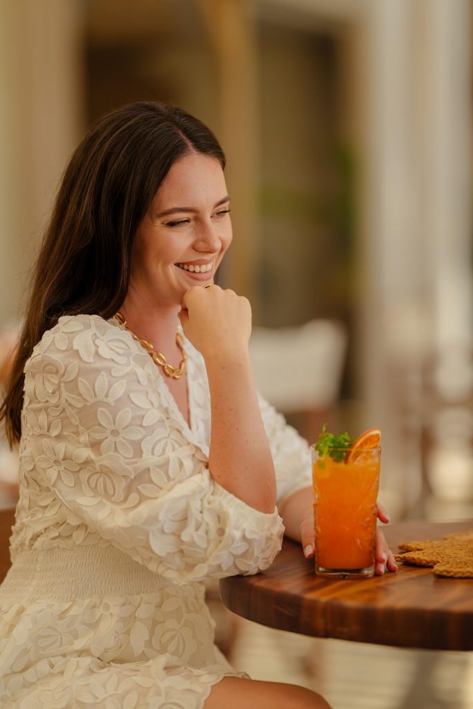 A women sitting at a table, smiling and drinking a cocktail