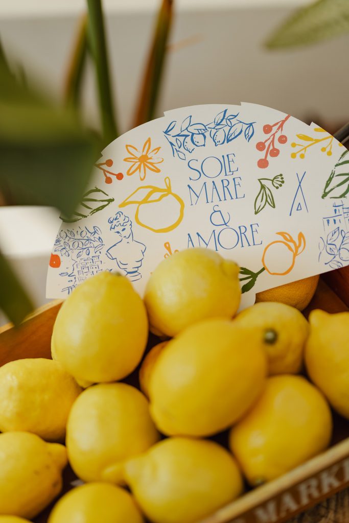 Bowl of fresh lemons with a decorative card featuring colourful illustrations and the text “Sole Mare & Amore” in the background