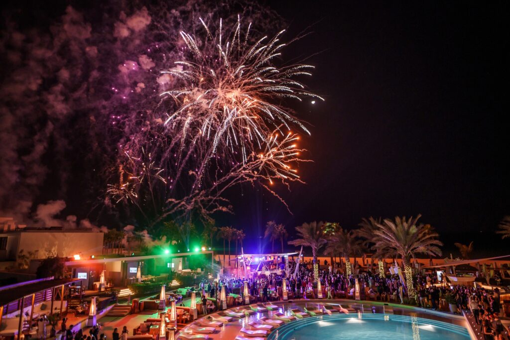 Colorful fireworks illuminate the night sky above a shimmering pool and beach, celebrating a vibrant New Year at Nikki Beach Dubai