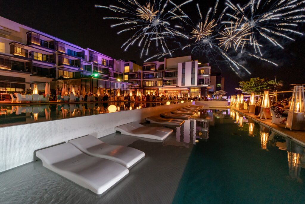 Fireworks illuminate the night sky above a luxurious hotel pool, celebrating the New Year in a coastal elegance setting
