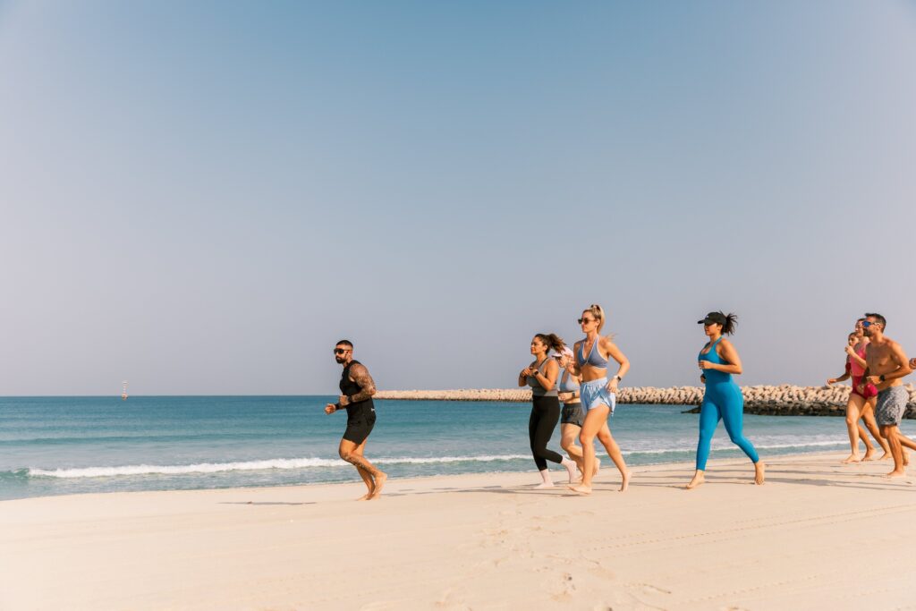 A group of people joyfully running on the beach, embracing fitness and the holiday spirit at Nikki Beach Resort & Spa