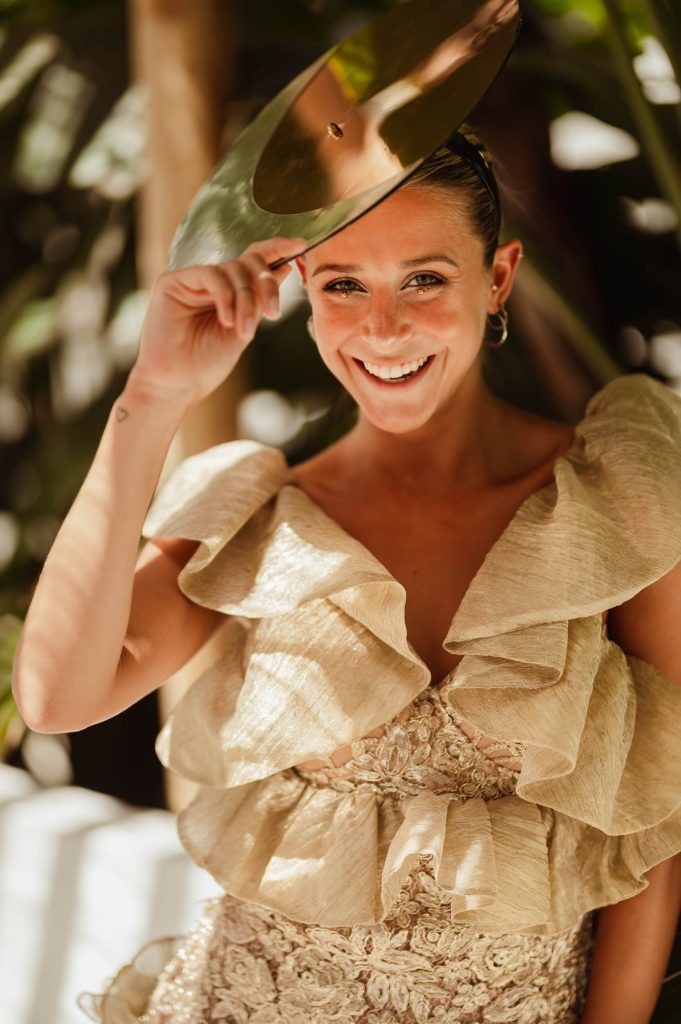 A lady smiling, shielding her face from the sun with a headdress