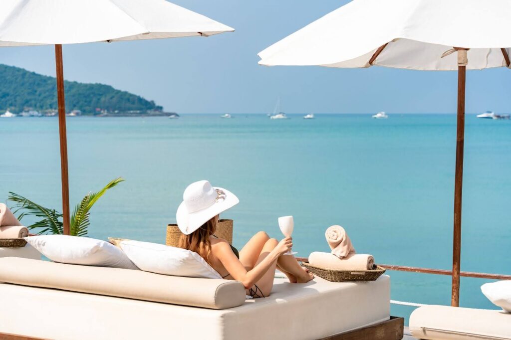 A fashionable woman in a white hat lounges under white umbrellas, enjoying a luxurious 4th of July at Nikki Beach