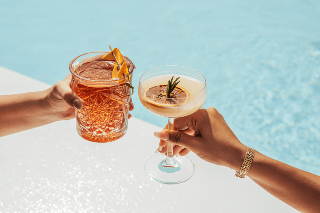 A stylish couple raises their cocktail glasses near a sparkling pool, embodying the festive spirit
