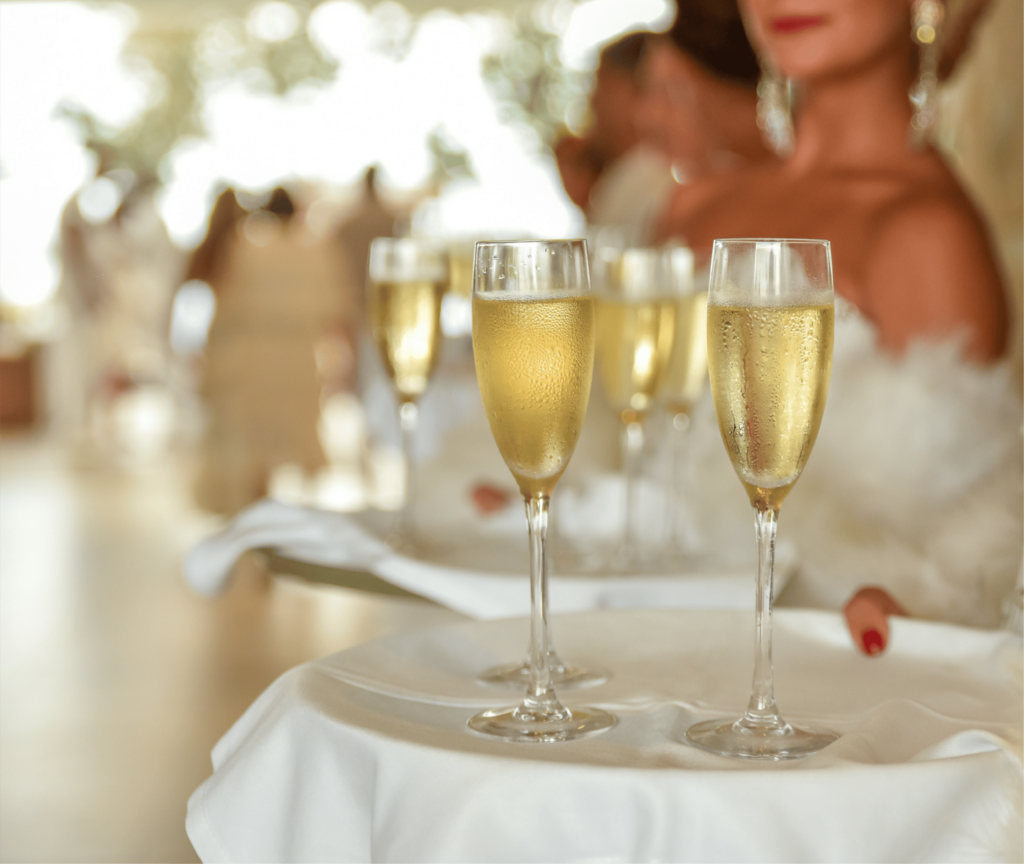A graceful woman in a white dress holds a tray of champagne glasses, celebrating the joyous holiday spirit by the ocean