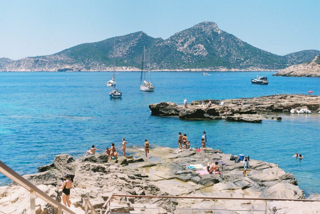Costal image of people sunbathing on the rocks and small boats near the shore