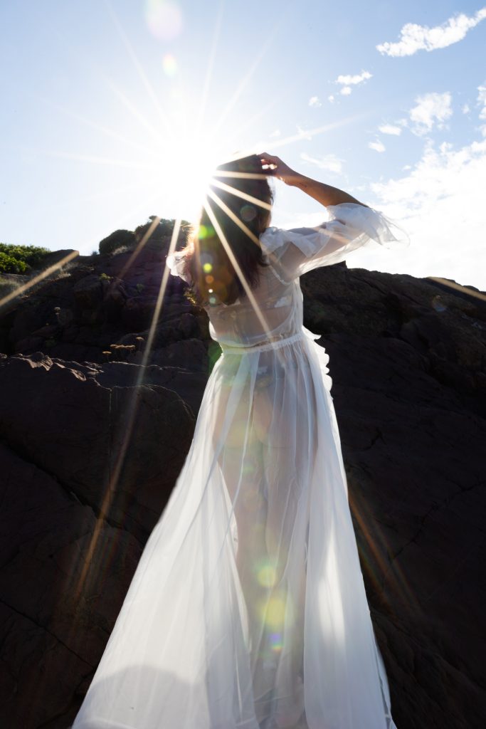 A lady standing in the sunlight in a flowing white beach cover up dress