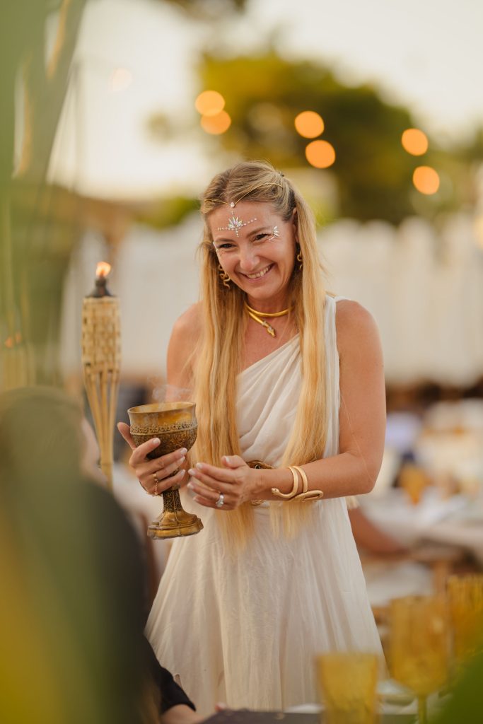 Lady holding a gold goblet cup, wearing face paint, smiling off camera