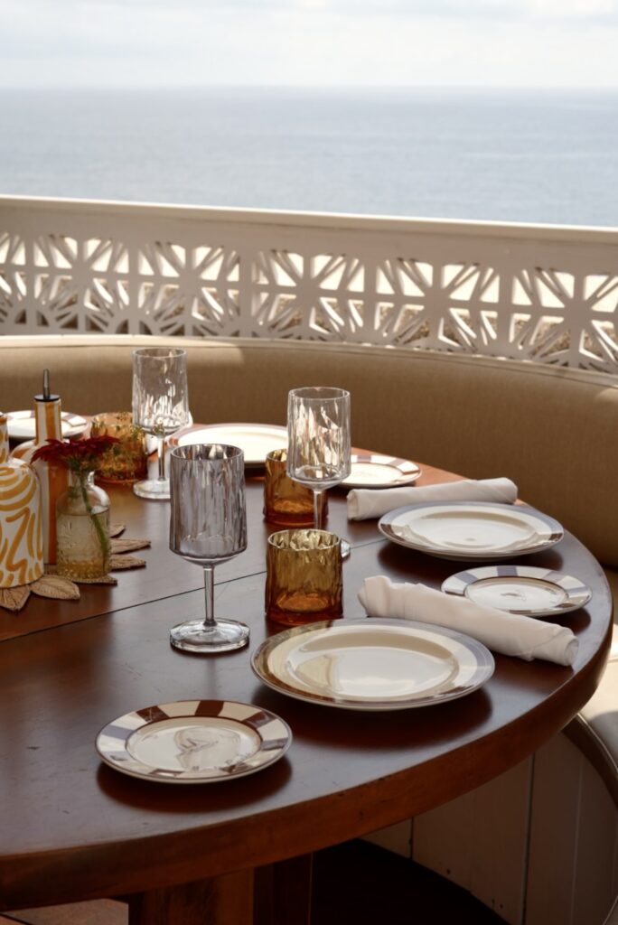 A table looking out to the sea, the table is set with plates, cutlery and wine glasses
