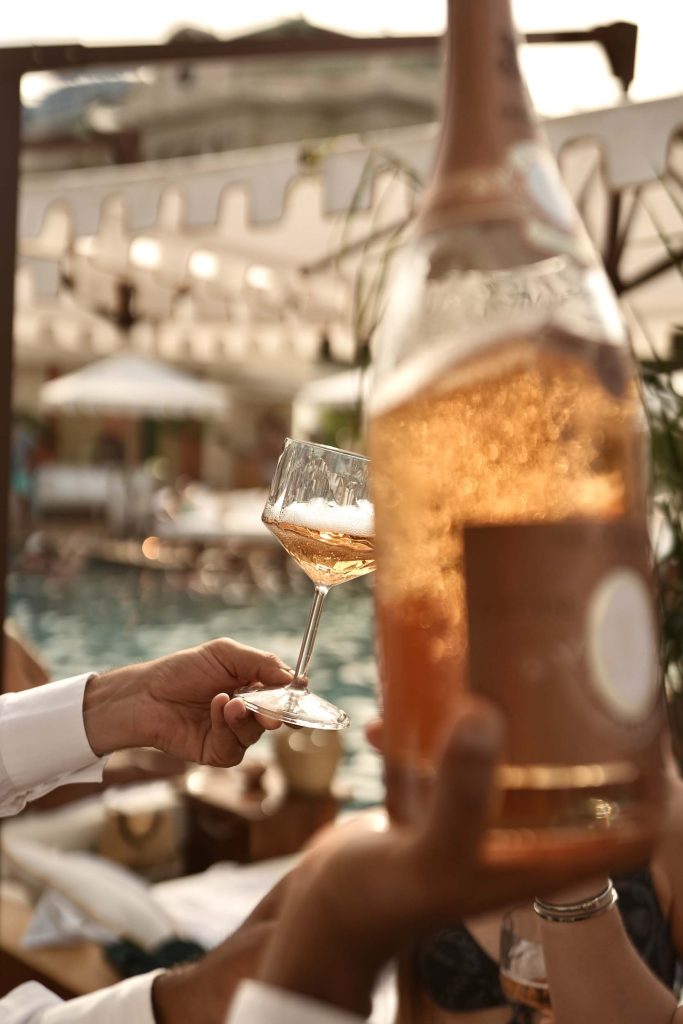 A person holding a glass of sparkling wine with a bottle held at the front of the frame