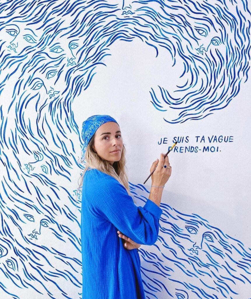 Dothy Henriot, founder of Mersea People, posing with a paintbrush and mural