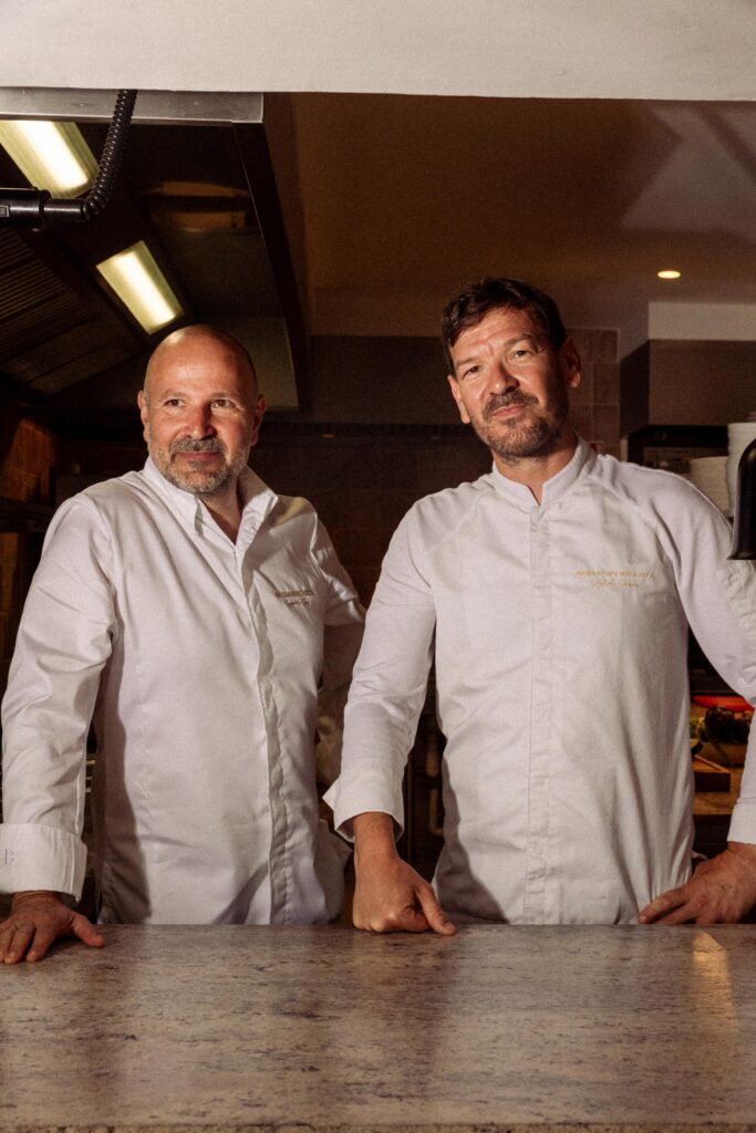 Two chefs posing for the camera, leaning on a counter