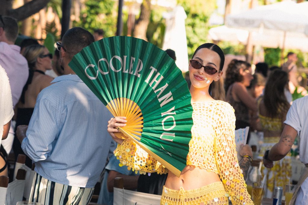 Young lady holding an oversized handheld fan with "cooler than you" across the open fan