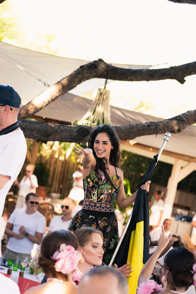 A women entertaining Nikki Beach guests in a colourful dress, pointing and smiling at guests
