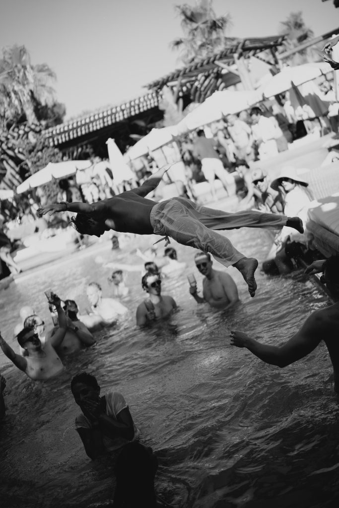 man jumping into a pool in black and white, with people in the pool