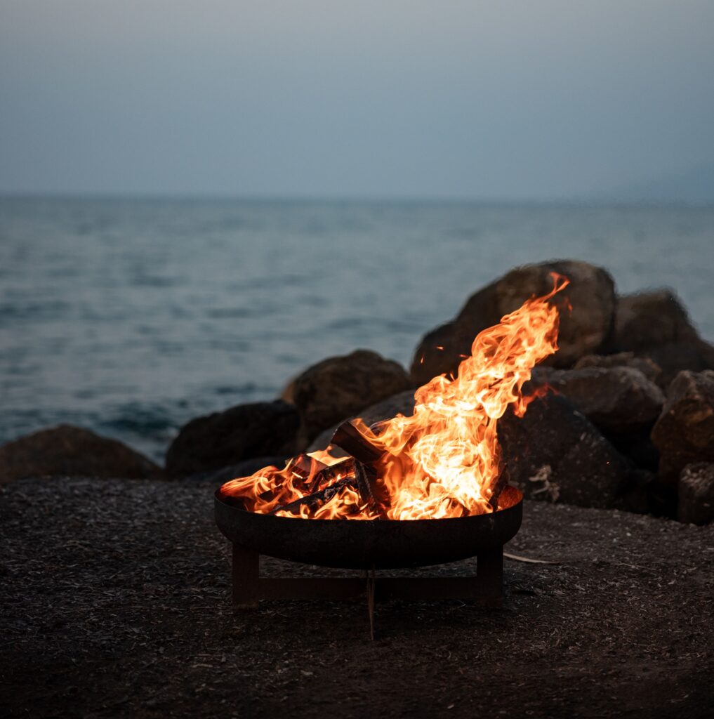 A cozy fire pit on the beach, with the ocean waves gently lapping nearby, perfect for a moonlit dinner experience